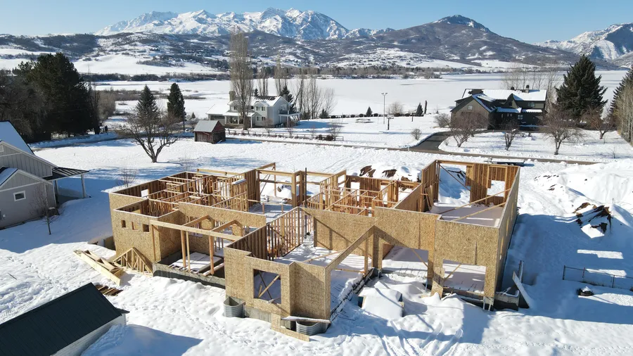 Custom home framing underway in deep snow with the Ogden Valley and mountains behind