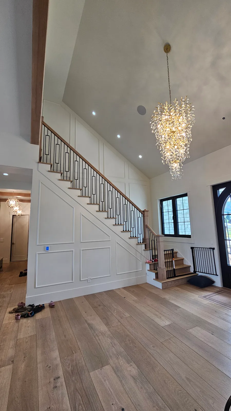 Completed two-story entry foyer with wood staircase, iron balusters, wainscoting, and chandelier